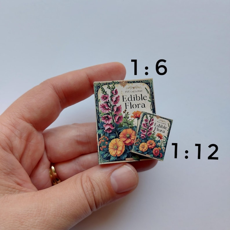 Puede incluir: Dos libros en miniatura con el t&iacute;tulo "Edible Flora" e ilustraciones florales. Los libros se sostienen en una mano. Las ilustraciones presentan flores rosas, naranjas y amarillas. El texto "Edible Flora" es visible.