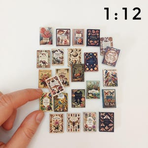 Puede incluir: Una colecci&oacute;n de 20 libros en miniatura con diversas ilustraciones de tem&aacute;tica natural, incluyendo p&aacute;jaros, flores, insectos y hongos. Los libros est&aacute;n dispuestos en una cuadr&iacute;cula sobre una superficie blanca. El texto "1:12" es visible en la esquina superior derecha de la imagen.