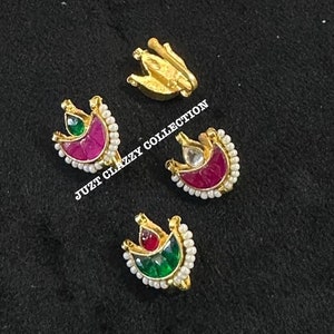 May include: Three gold nose rings with red and green gemstones and white pearl accents. The nose rings are in the shape of a crescent moon with a teardrop-shaped gemstone in the center. "Juzt Clazzy Collection" is written in white text on a black background.