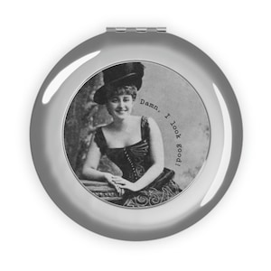 Könnte beinhalten: Ein runder, silberner Kompaktspiegel mit einem Schwarz-Weiß-Bild einer Frau in Vintage-Kleidung. Das Bild enthält den Text "Damn, I look good!" in einem kreisförmigen Muster.