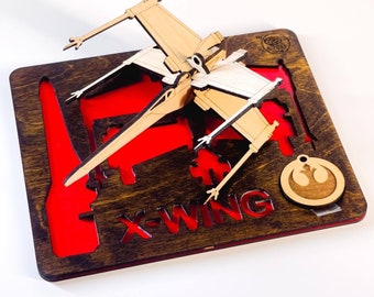 May include: A wooden X-Wing Starfighter model with a red background and the text "X-WING" on the base. The model is made of laser-cut wood and has a white and brown color scheme. The model is a popular collectible for Star Wars fans.