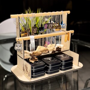 以下が含まれることがあります： 猫をテーマにしたネックレスやキーホルダーが並んだ木製ディスプレイスタンド。スタンドは2段になっており、「The Tree Lab」の文字が飾られています。