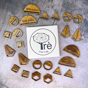 Op de afbeelding: Assortiment van houten oorbellen in verschillende vormen en maten. De oorbellen hebben de tekst "Tejidos Urbanos" en "Trè The Lab".