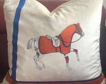 May include: A white pillow with a blue stripe down the side and a red, orange, and white horse illustration in the center. The horse is wearing a saddle and bridle.