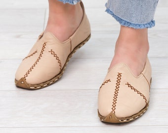 May include: A pair of light beige leather slip-on shoes with brown stitching. The shoes have a pointed toe and a flat sole.