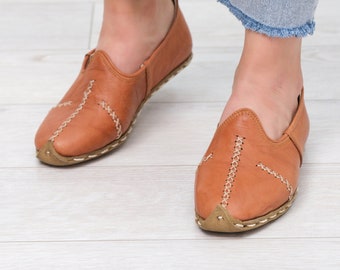 May include: A pair of brown leather slip-on shoes with white stitching. The shoes have a pointed toe and a flat sole.