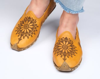 May include: A pair of yellow leather slip-on shoes with a black geometric design. The shoes have a pointed toe and a flat sole.
