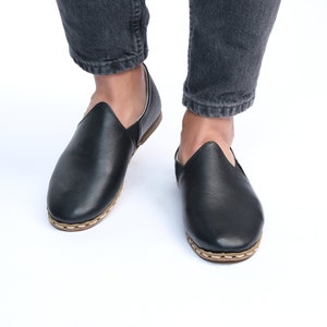 May include: A pair of black leather slip-on shoes with a stitched edge and a brown sole.