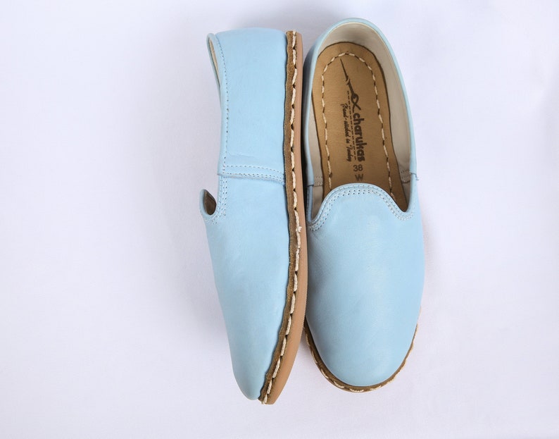 K&ouml;nnte beinhalten: Ein Paar hellblaue Lederschuhe zum Hineinschl&uuml;pfen mit brauner Ledersohle und wei&szlig;en N&auml;hten. Die Schuhe haben eine spitze Zehenpartie und eine bequeme Passform. Der Markenname "charukkas" ist auf der Innenseite des Schuhs aufgedruckt.
