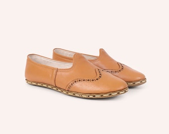 May include: A pair of tan leather slip-on shoes with a brogue design and a white stitch detail around the sole.