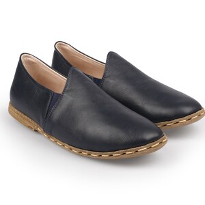 May include: A pair of dark blue leather slip-on shoes with a brown stitched sole.