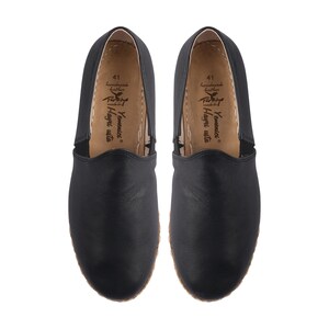 May include: A pair of black leather slip-on shoes with a brown leather insole. The insole has the text "Yamamoto" and "Hangri Walla" printed on it.