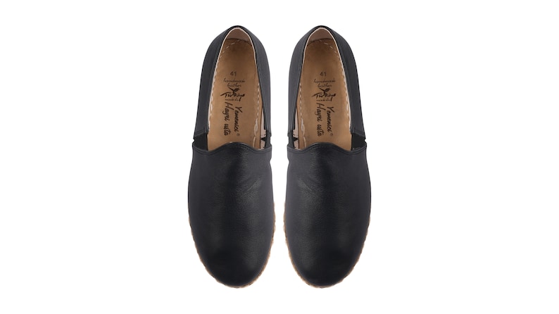 May include: A pair of black leather slip-on shoes with a brown leather insole. The insole has the text "Yamamoto" and "Hangri Walla" printed on it.