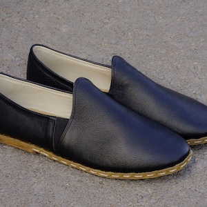 May include: A pair of black leather slip-on shoes with a stitched edge and a brown sole.