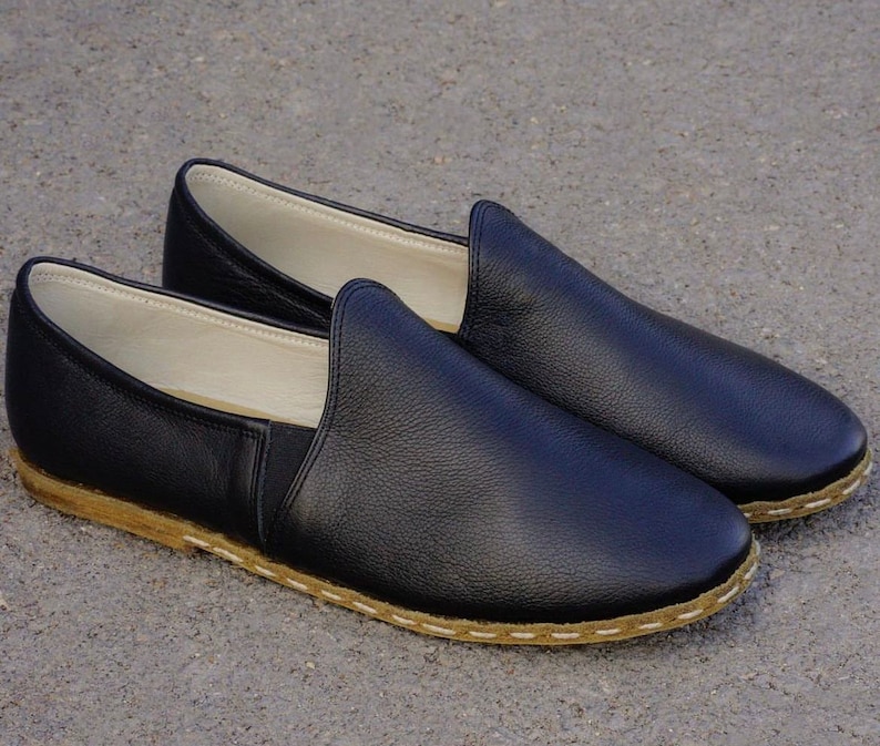 May include: A pair of black leather slip-on shoes with a stitched edge and a brown sole.
