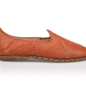 May include: A pair of orange leather slip-on shoes with a pointed toe and decorative stitching.