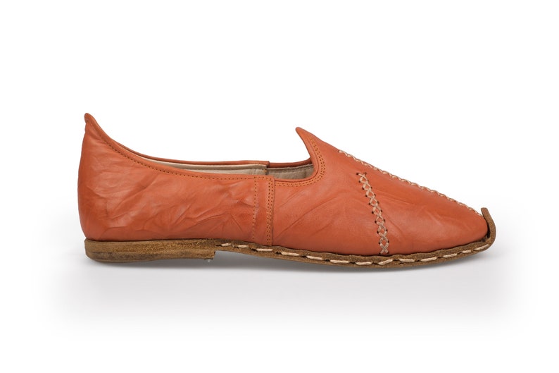 May include: A pair of orange leather slip-on shoes with a pointed toe and decorative stitching.