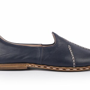 May include: A pair of navy blue leather slip-on shoes with a decorative stitch detail around the edges.