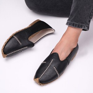 May include: A pair of black leather slip-on shoes with decorative stitching. The shoes have a pointed toe and a flat sole.