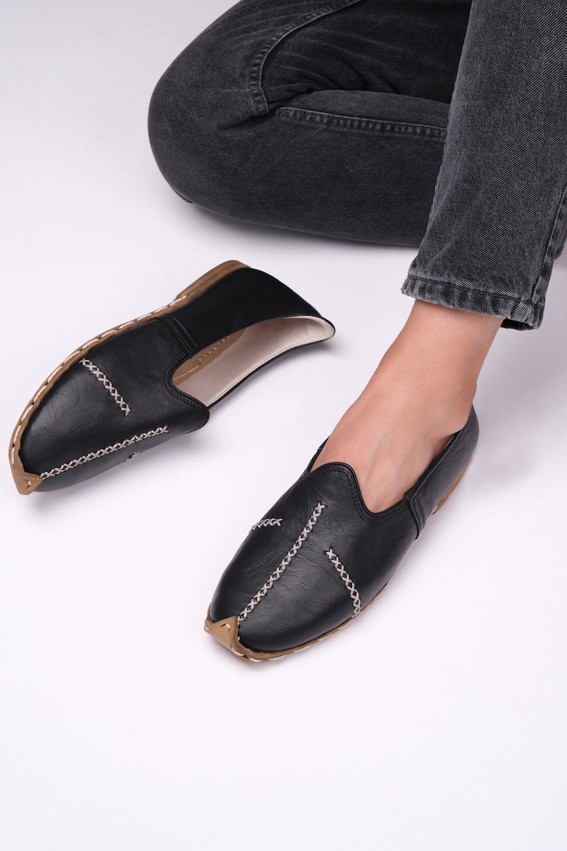 May include: A pair of black leather slip-on shoes with decorative stitching. The shoes have a pointed toe and a flat sole.