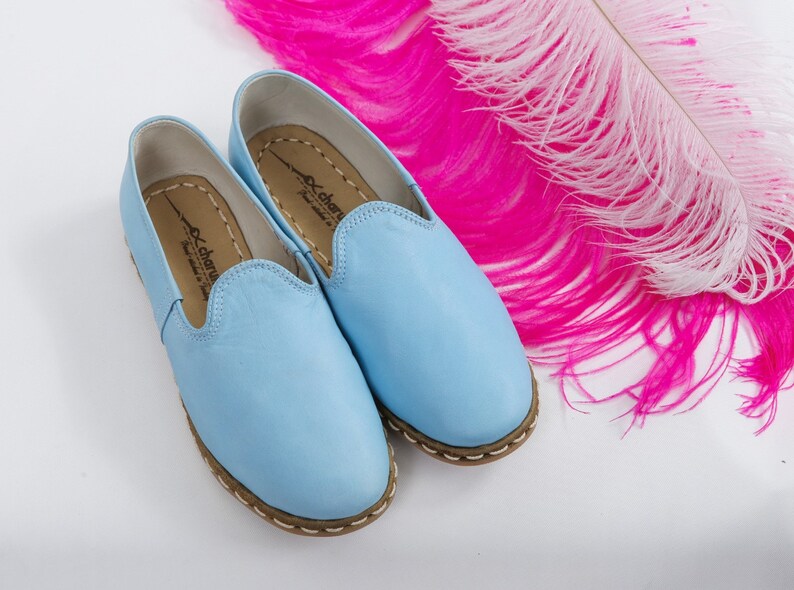 K&ouml;nnte beinhalten: Ein Paar hellblaue Lederschlappen mit braunem Steppsaum. Die Schuhe haben ein schlichtes Design und sind aus weichem Leder gefertigt.