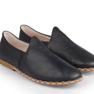May include: A pair of black leather slip-on shoes with a brown stitched trim.