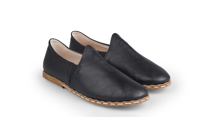 May include: A pair of black leather slip-on shoes with a brown stitched trim.