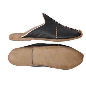 May include: Black leather slippers with a white stitch detail and a brown leather sole.