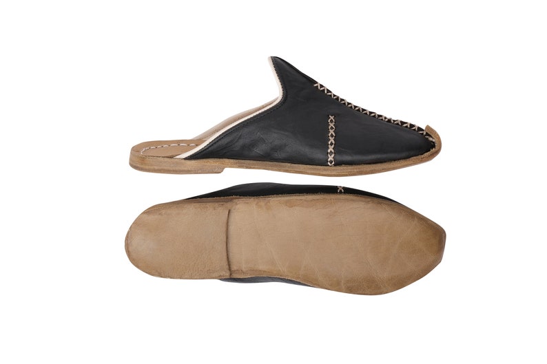 May include: Black leather slippers with a white stitch detail and a brown leather sole.