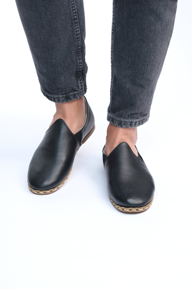 May include: A pair of black leather slip-on shoes with a stitched edge and a brown sole.
