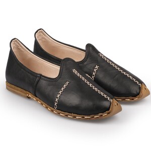 May include: A pair of black leather slip-on shoes with a brown stitched trim. The shoes have a pointed toe and a flat sole.