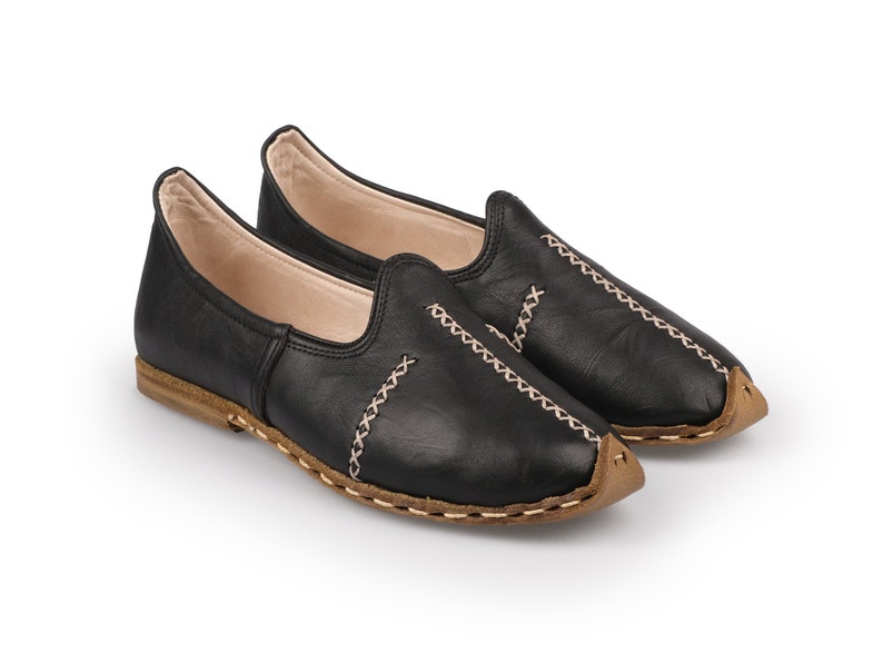 May include: A pair of black leather slip-on shoes with a brown stitched trim. The shoes have a pointed toe and a flat sole.