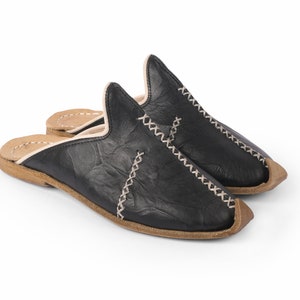 May include: A pair of black leather slippers with a white stitch detail and a brown leather sole.