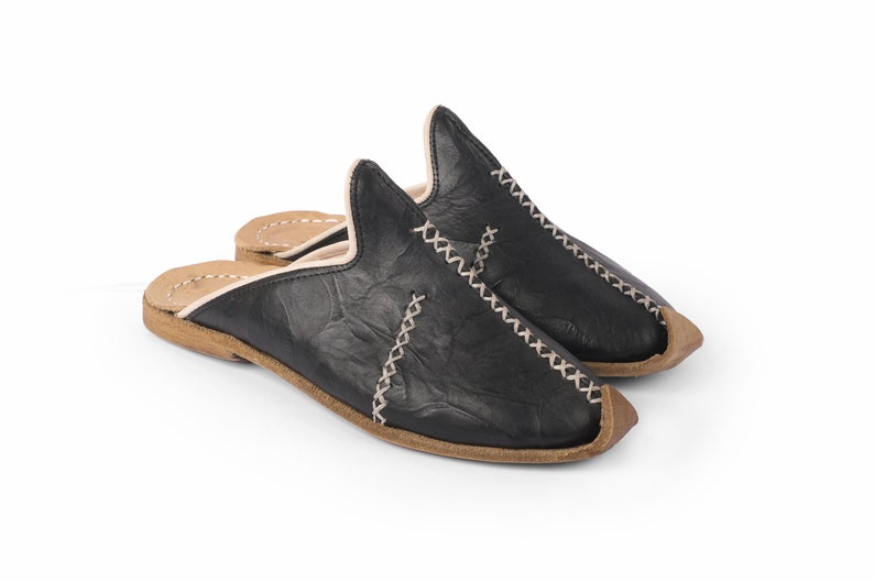 May include: A pair of black leather slippers with a white stitch detail and a brown leather sole.