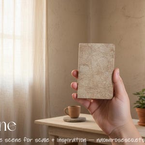 May include: A rectangular notebook with a textured, light beige cover featuring a marbled, organic pattern. The notebook is held upright, displaying its front cover. The text 'Jayne' is printed in white in the lower left corner of the image.