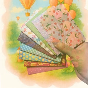 May include: A fan of rectangular paper sheets featuring diverse patterns including cherries, butterflies, gingham, polka dots, and glittery textures, displayed against a background illustration of hot air balloons and the text Balloon Orchard.