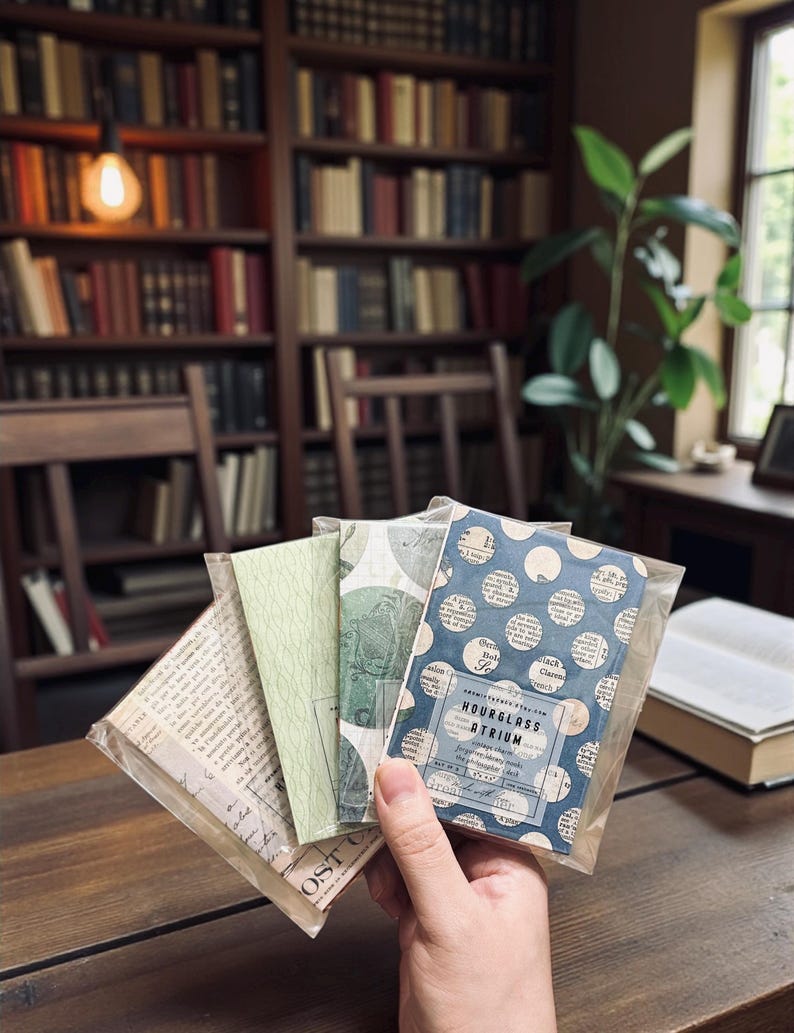 May include: A set of four rectangular paper ephemera packs in clear plastic sleeves. The front pack features a blue and white polka dot pattern over vintage newspaper text with a label reading Hourglass Atrium. Other packs show green botanical prints.