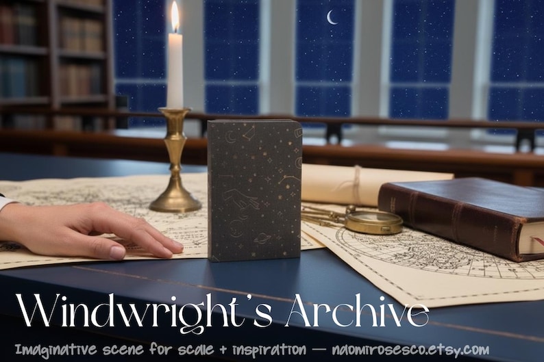 May include: A dark gray rectangular book featuring gold celestial illustrations of stars, moons, and constellations on the cover. The book is positioned upright on a surface alongside a brass candle holder with a lit candle, a compass, and maps.