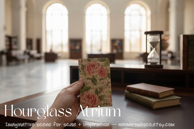 May include: A small rectangular card featuring a vintage-style floral pattern with pink roses and green leaves on a cream background with subtle text, held in front of a blurred library interior with an hourglass and two stacked books.