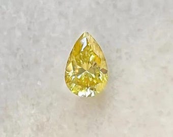 May include: A pear-shaped, fancy vivid yellow diamond. The gemstone is faceted, with a brilliant cut that reflects light. The diamond is set against a white background, highlighting its color and clarity. This gemstone is suitable for jewelry.