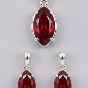 May include: A jewelry set featuring a pendant necklace and matching earrings. The set includes a silver-toned chain and settings, with marquise-cut, faceted, deep red gemstones. The pendant and earrings have a similar design, with the gemstones held in place by four prongs.