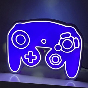 May include: A blue and white GameCube controller shaped night light. The controller is lit up with a blue glow.