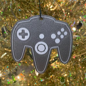 May include: A gray and white Nintendo 64 controller ornament. The controller is a popular video game console accessory and is a great gift for gamers.