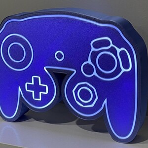 May include: A blue 3D printed GameCube controller lamp with white outlines. The lamp is lit up with a blue glow.