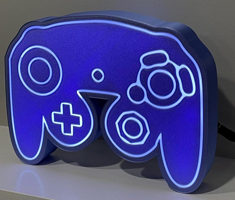 May include: A blue 3D printed GameCube controller lamp with white outlines. The lamp is lit up with a blue glow.