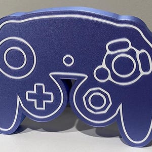 May include: A blue GameCube controller shaped night light with white outlines. The light is plugged in with a black cord.