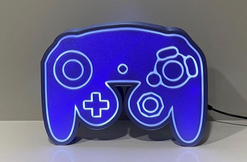 May include: A blue and white GameCube controller shaped night light. The controller is lit up with a white glow.