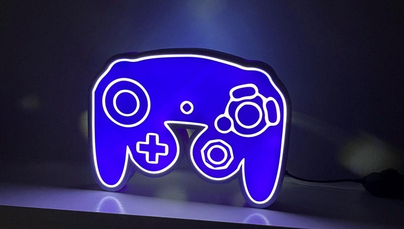 May include: A blue and white GameCube controller shaped night light. The controller is lit up with a blue glow.