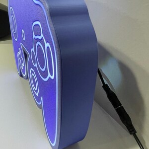 May include: A purple and blue 3D printed GameCube controller night light with a white cord.