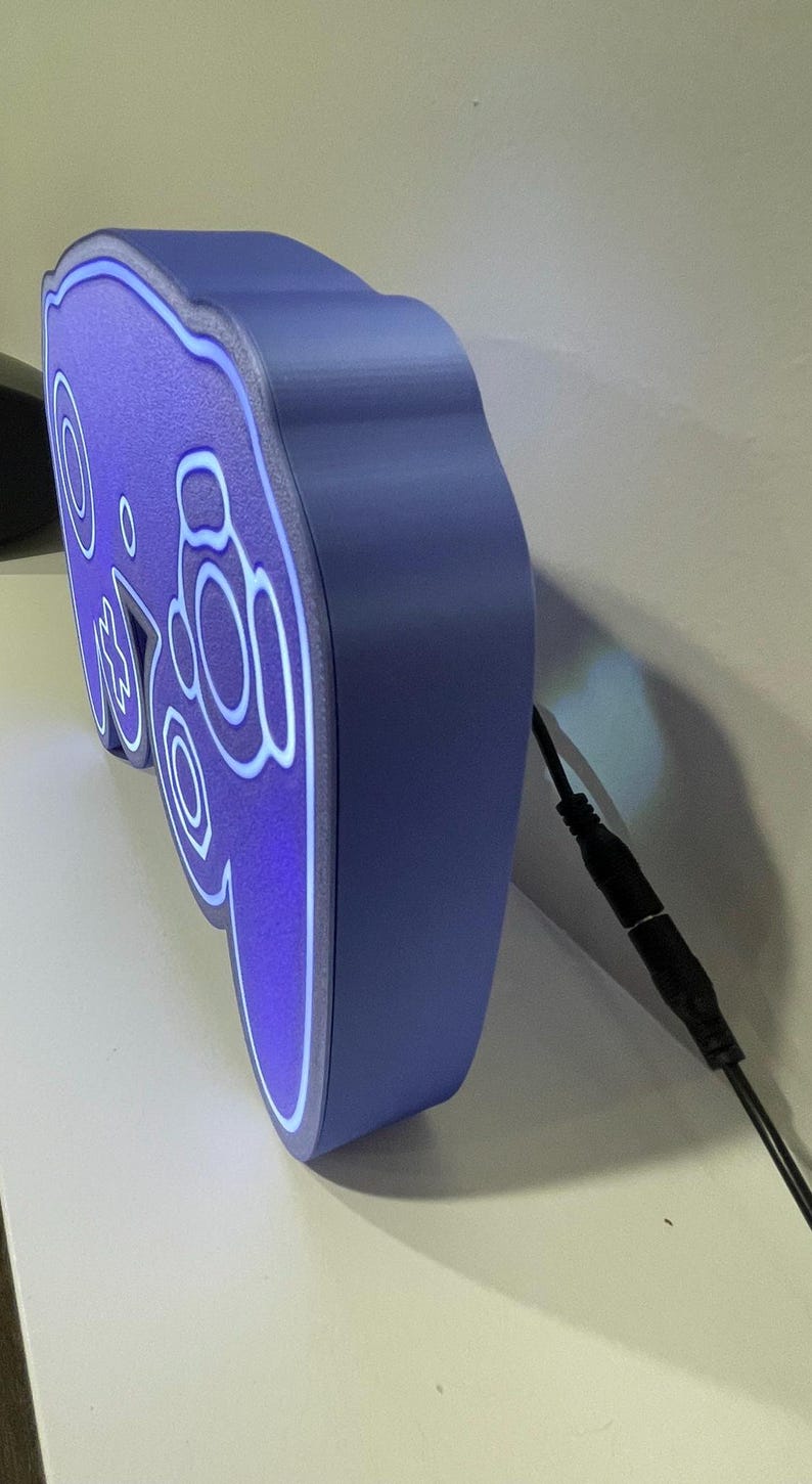May include: A purple and blue 3D printed GameCube controller night light with a white cord.